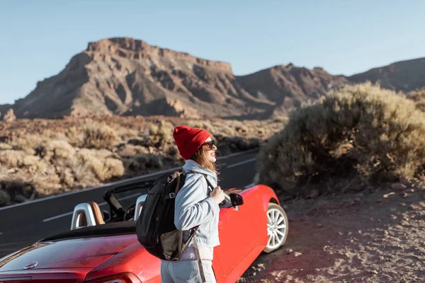 Woman traveling by the red car on a desert road — Zdjęcie stockowe