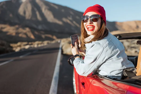 Woman leaning out of the car with smartphone on the roadside — Zdjęcie stockowe