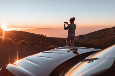 Woman enjoying beautiful sunset while traveling in the mountains by car
