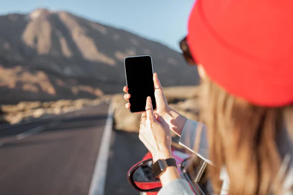 Woman leaning out of the car with smartphone on the roadside — Stockfoto
