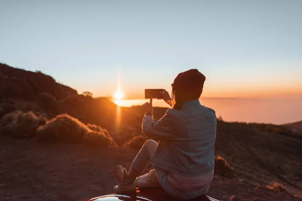 En kvinne som nyter en vakker solnedgang mens hun reiser i fjellet med bil – stockfoto