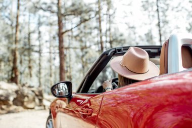 Woman driving a cabriolet while traveling in the forest