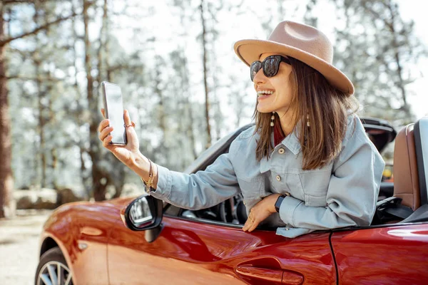 Mujer fotografiando por teléfono mientras viaja en coche en el bosque — Foto de Stock