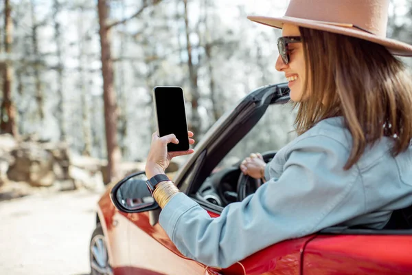 Жінка фотографує по телефону під час подорожі на машині в лісі — стокове фото