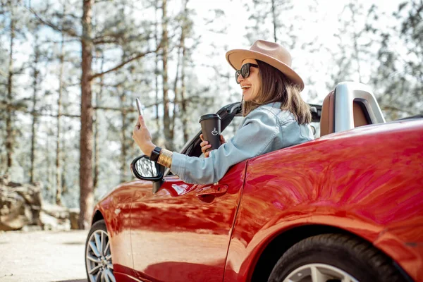 Mujer fotografiando por teléfono mientras viaja en coche en el bosque — Foto de Stock