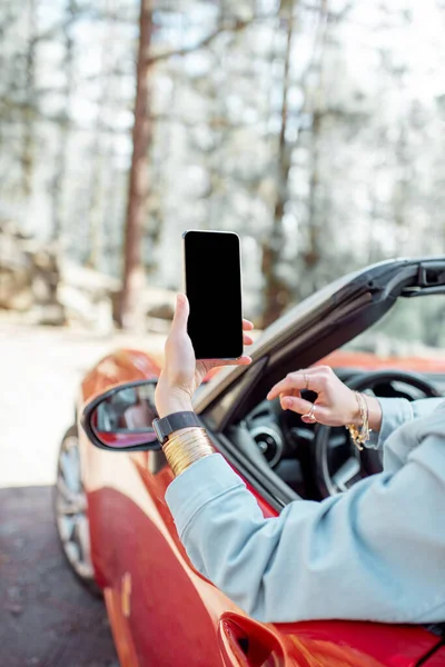 Mujer fotografiando por teléfono mientras viaja en coche en el bosque — Foto de Stock