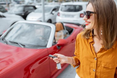 Happy woman with keys near the car at the parking