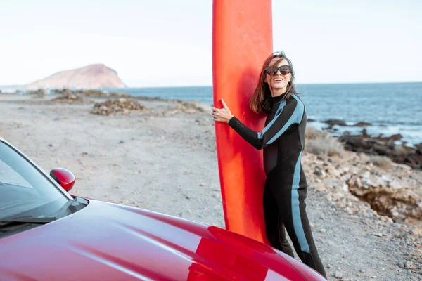 Young woman with surfboard on the rocky coast — Stockfoto