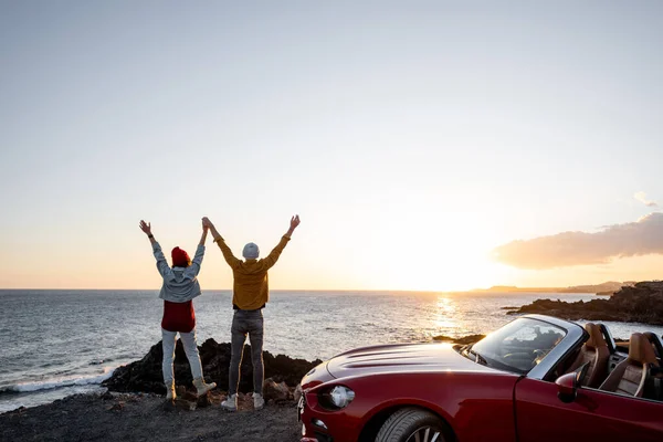 Härligt par på stranden nära bilen på en solnedgång — Stockfoto