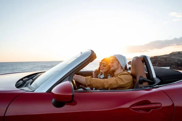 Lovely couple driving a cabriolet on a sunset — Stockfoto