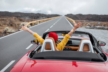 Cabriolet arabasıyla volkanik vadide seyahat eden bir kadın.
