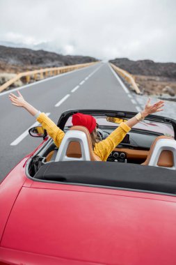 Cabriolet arabasıyla volkanik vadide seyahat eden bir kadın.