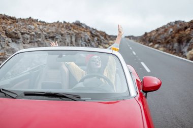 Cabriolet arabasıyla volkanik vadide seyahat eden bir kadın.