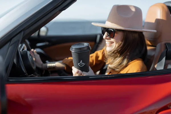 Nainen, jolla on kahvikuppi ajamassa Cabrioletilla lähellä merta. — kuvapankkivalokuva