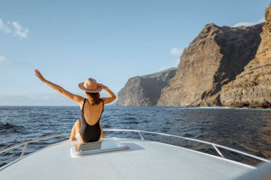 Kayalık sahilin yakınındaki yatta yelken açan bir kadın.