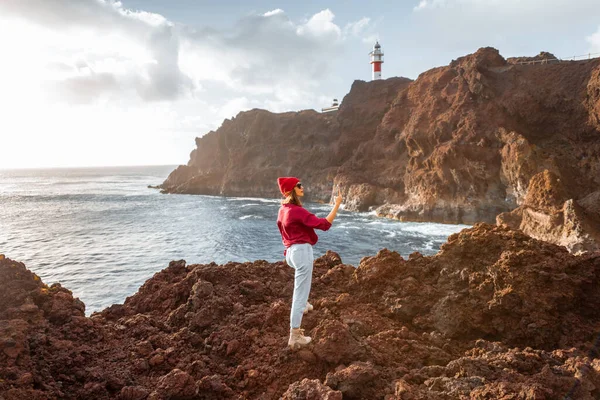 Женщина, путешествующая по скалистому океану возле маяка — стоковое фото