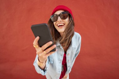 Dışarıdaki kırmızı arka planda telefonu olan kadın.