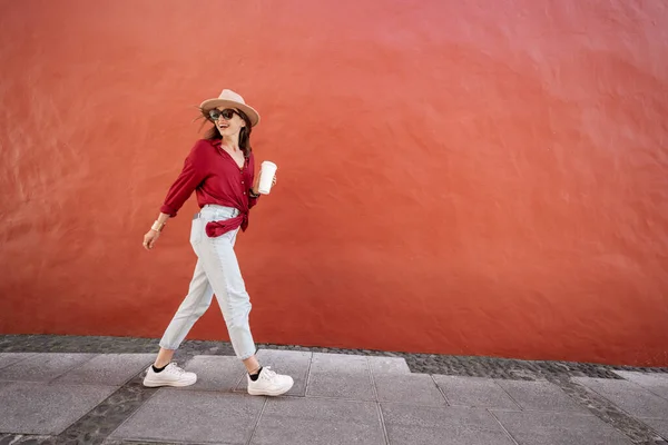 Potret seorang wanita bergaya dengan cangkir kopi di latar belakang dinding merah — Stok Foto