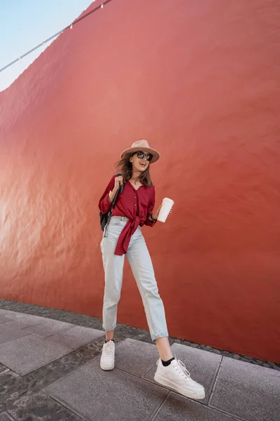 Portrét stylové ženy s šálkem kávy na červeném pozadí zdi — Stock fotografie