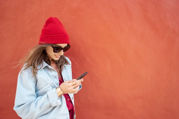 Vrouw met telefoon op de rode achtergrond buiten — Stockfoto