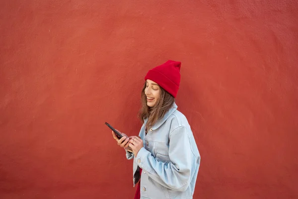 Vrouw met telefoon op de rode achtergrond buiten — Stockfoto