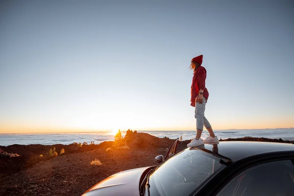 Frau, die mit dem Auto im felsigen Gelände über den Wolken unterwegs ist, bei Sonnenuntergang — Stockfoto