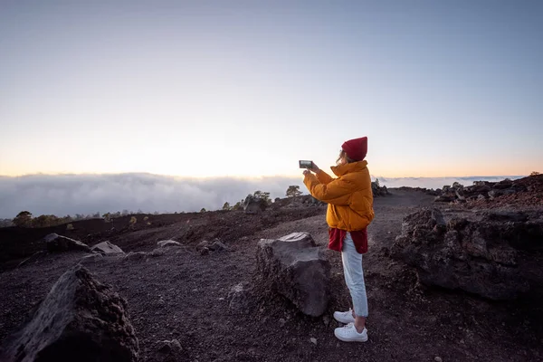 Žena putující po skalách nad mraky při západu slunce — Stock fotografie