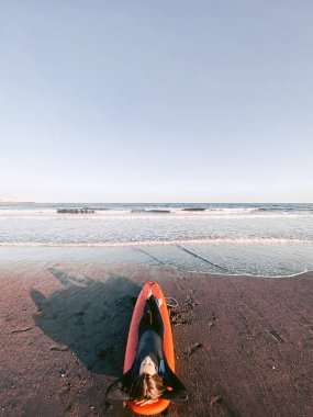 Relaxed surfer in wetsuit sitting on the surfboard on the beach