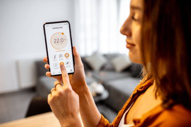 Woman controlling heating with a smart phone at home