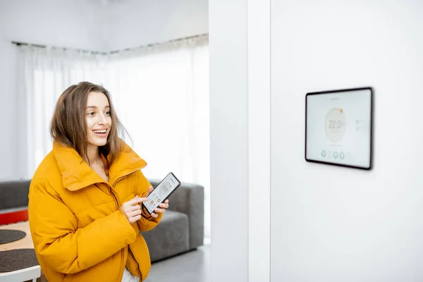 Cold woman controlling heating with a smart devices — Stockfoto