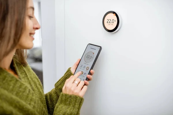 Mujer que regula la temperatura de calefacción con teléfono y termostato en casa — Foto de Stock