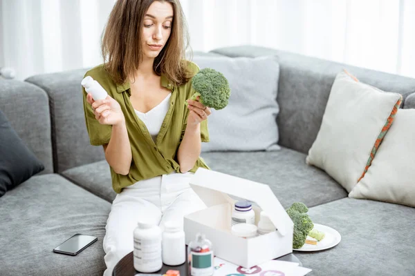 Thoughtful woman with nutritional supplements and broccoli at home — 图库照片