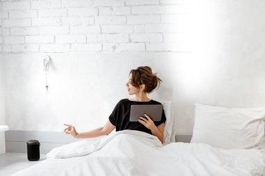 Woman relaxing with a smart speaker and tablet in the bedroom
