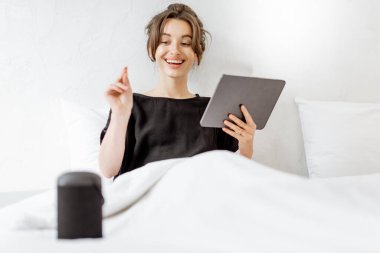 Woman relaxing with a smart speaker and tablet in the bedroom