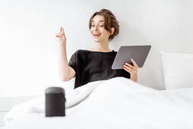 Woman relaxing with a smart speaker and tablet in the bedroom