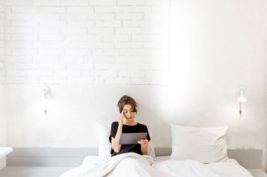 Woman relaxing with a digital tablet in the bedroom