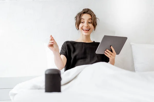 Woman relaxing with a smart speaker and tablet in the bedroom — Stockfoto