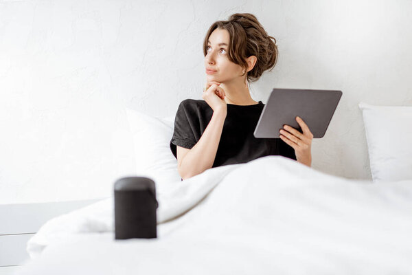 Woman relaxing with a smart speaker and tablet in the bedroom