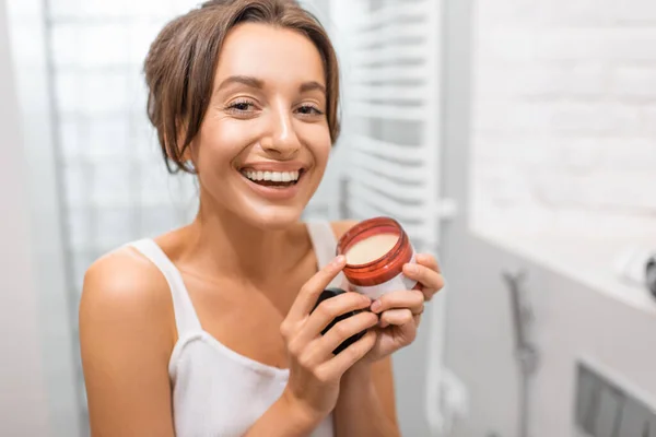 Femme avec crème faciale dans la salle de bain — Photo