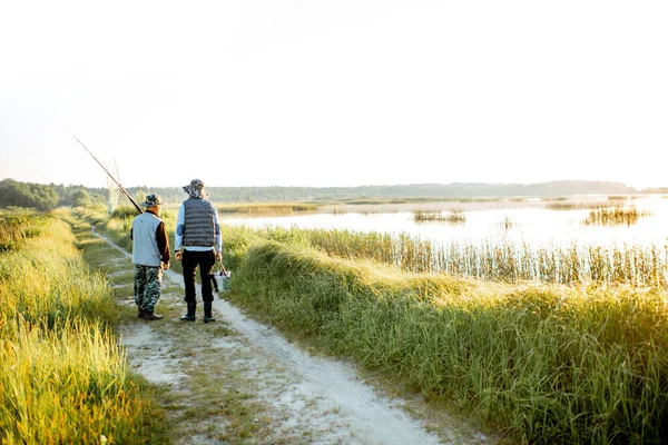 Дедушка со взрослым сыном прогуливается у озера — стоковое фото