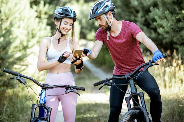 Hombre y mujer ciclistas con smartphone en la carretera forestal — Foto de Stock