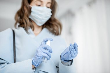 Tıbbi maskeli ve eldivenli bir kadın eve geldikten sonra ellerini dezenfekte ediyor.