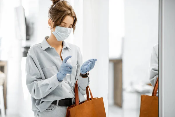 Mulher em máscara médica e luvas desinfetando as mãos depois de chegar em casa — Fotografia de Stock