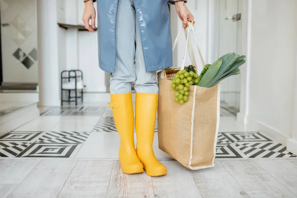 Mulher em botas de borracha amarela e capa de chuva com compras dentro de casa — Fotografia de Stock