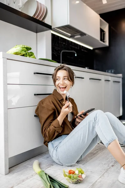 Mulher com comida saudável e telefone celular no chão da cozinha — Fotografia de Stock