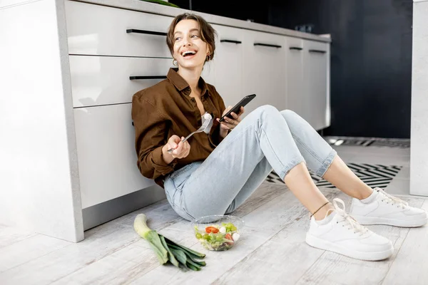 Woman with healthy food and mobile phone on the kitchen floor