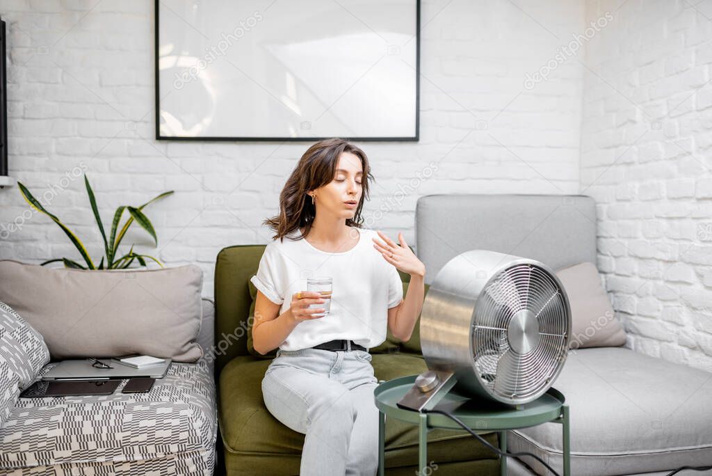 Woman cooling herself with a fan at home