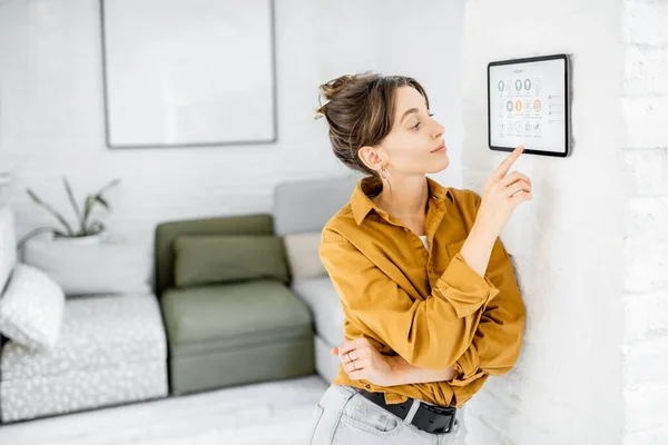 Kvinnan kontrollerar hemmet med en digital pekskärm — Stockfoto
