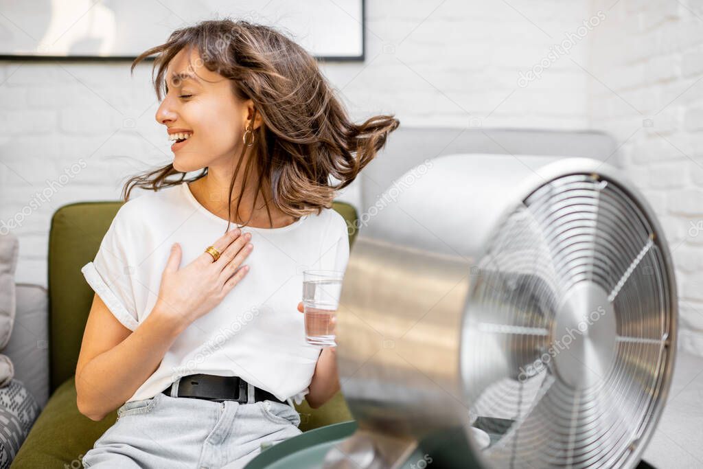 Woman cooling herself with a fan at home
