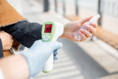 Dışarıdaki bir kontrol noktasında yüz maskesi takmış genç bir kadının vücut ısısını ölçüyorum.